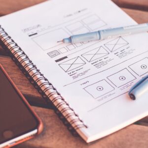 Close-up of a notebook with wireframe sketches and a smartphone on a wooden desk.